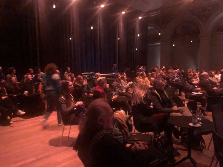 A large group of people sitting in a hall (cabaret set-up)